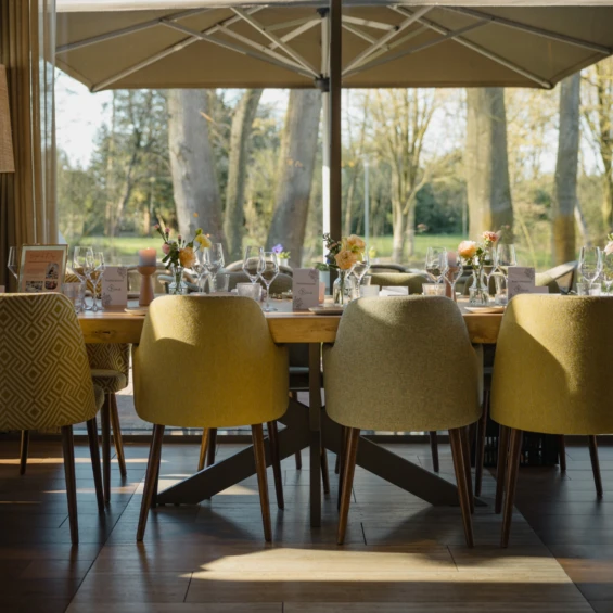 Lange gedekte tafel bij de ramen van Brasserie Jacob van Bijstervelt, met okergele stoelen en uitzicht op het park