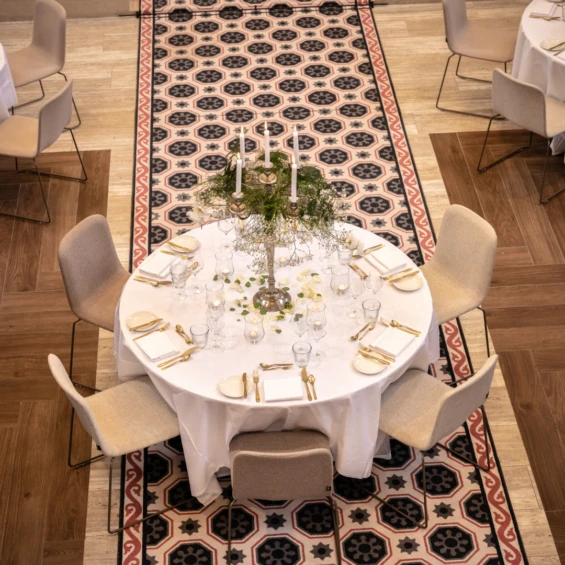 Ronde gedekte tafel met wit tafellinnen, gouden bestek en kandelaars, in een zaal met historische tegelvloer