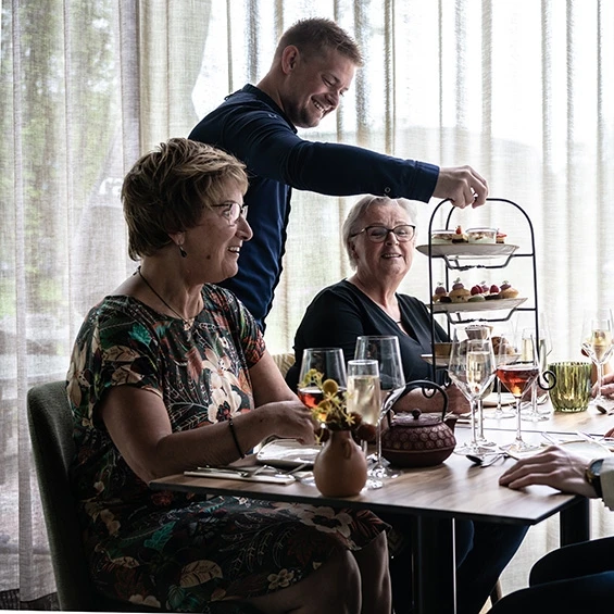 Medewerker serveert een etagère met zoete lekkernijen aan twee gasten tijdens de high tea