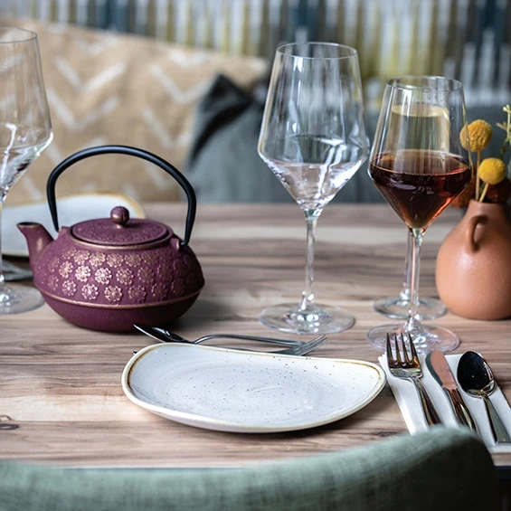 Gedekte tafel met gietijzeren theepot, wijnglazen en een vaasje gele bloemen