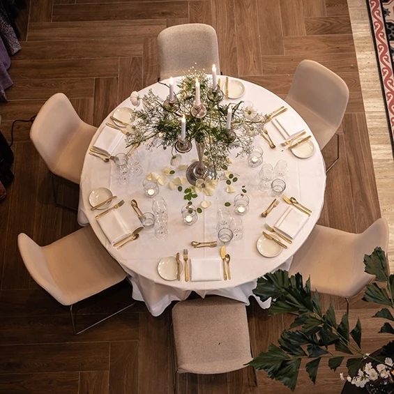 Ronde gedekte tafel van bovenaf, met wit linnen, gouden bestek en een kandelaar met groen