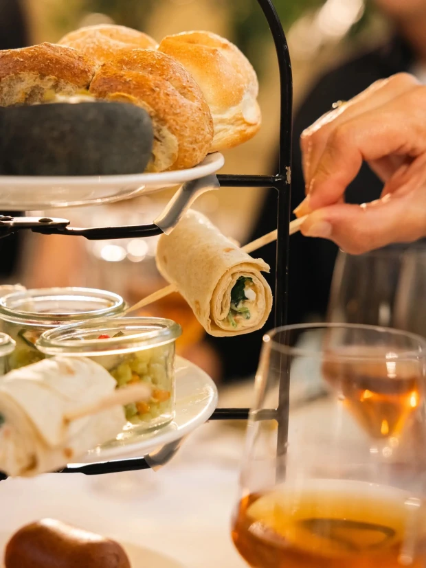Etagère van de high tea van dichtbij: broodjes bovenin, wraps aan een prikker en glaasjes met groentesalade.